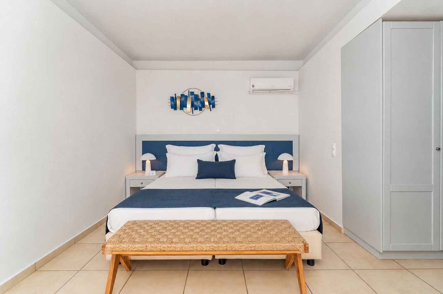 A modern bedroom with a bed, bedside tables, a bench, and a wall-mounted air conditioner.