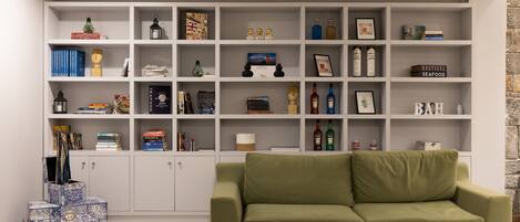 Una sala de estar con un sofá verde, una estantería blanca llena de libros y objetos decorativos, y una pared de piedra.