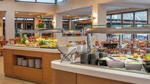 A buffet with various fruits and vegetables, a glass display case, and a seating area with tables and chairs. - Ariadne Beach - Adults Only (Agios Nikolaos)