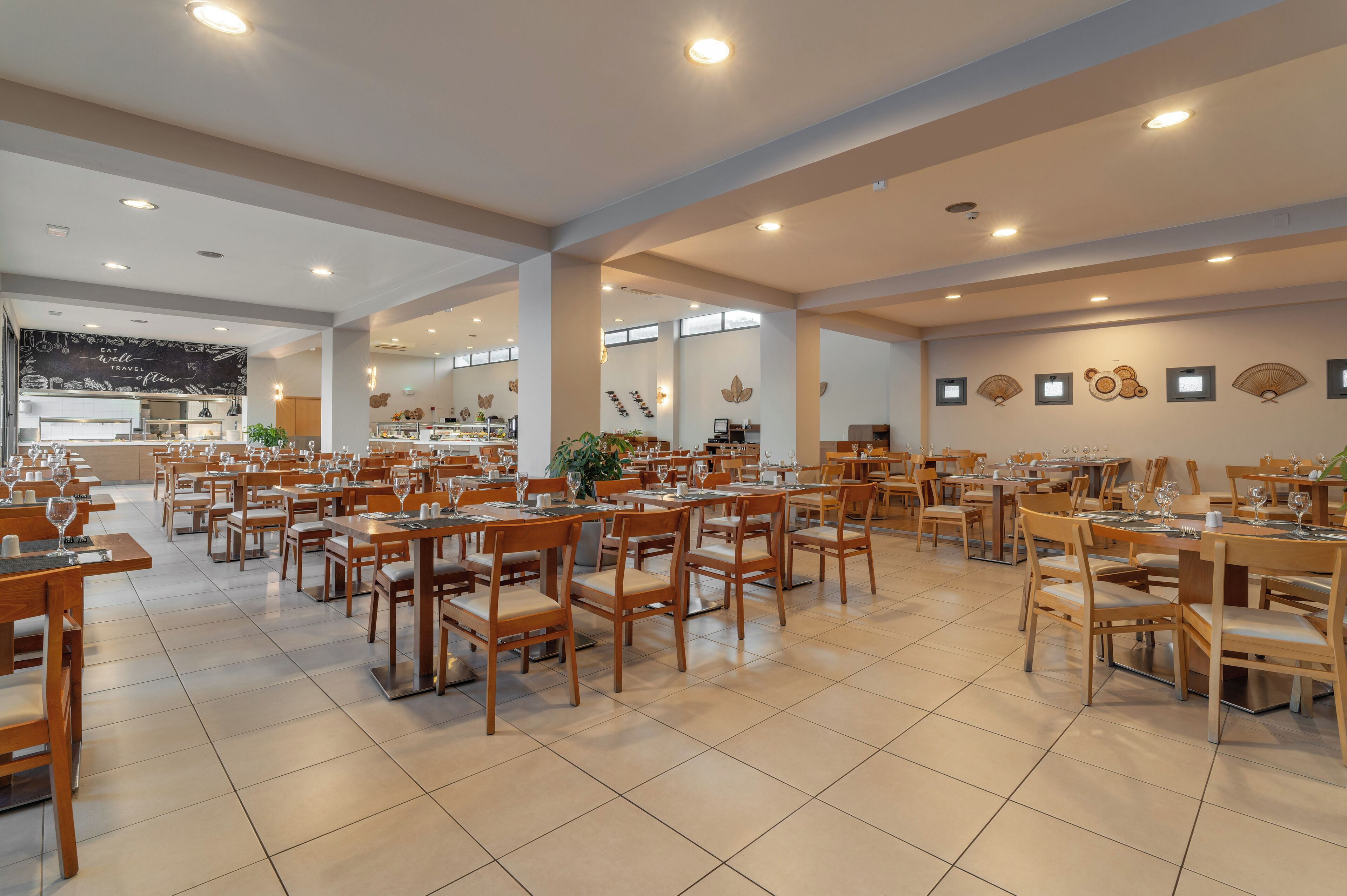 A spacious dining area with multiple tables and chairs, a kitchen in the background, and decorative wall art.