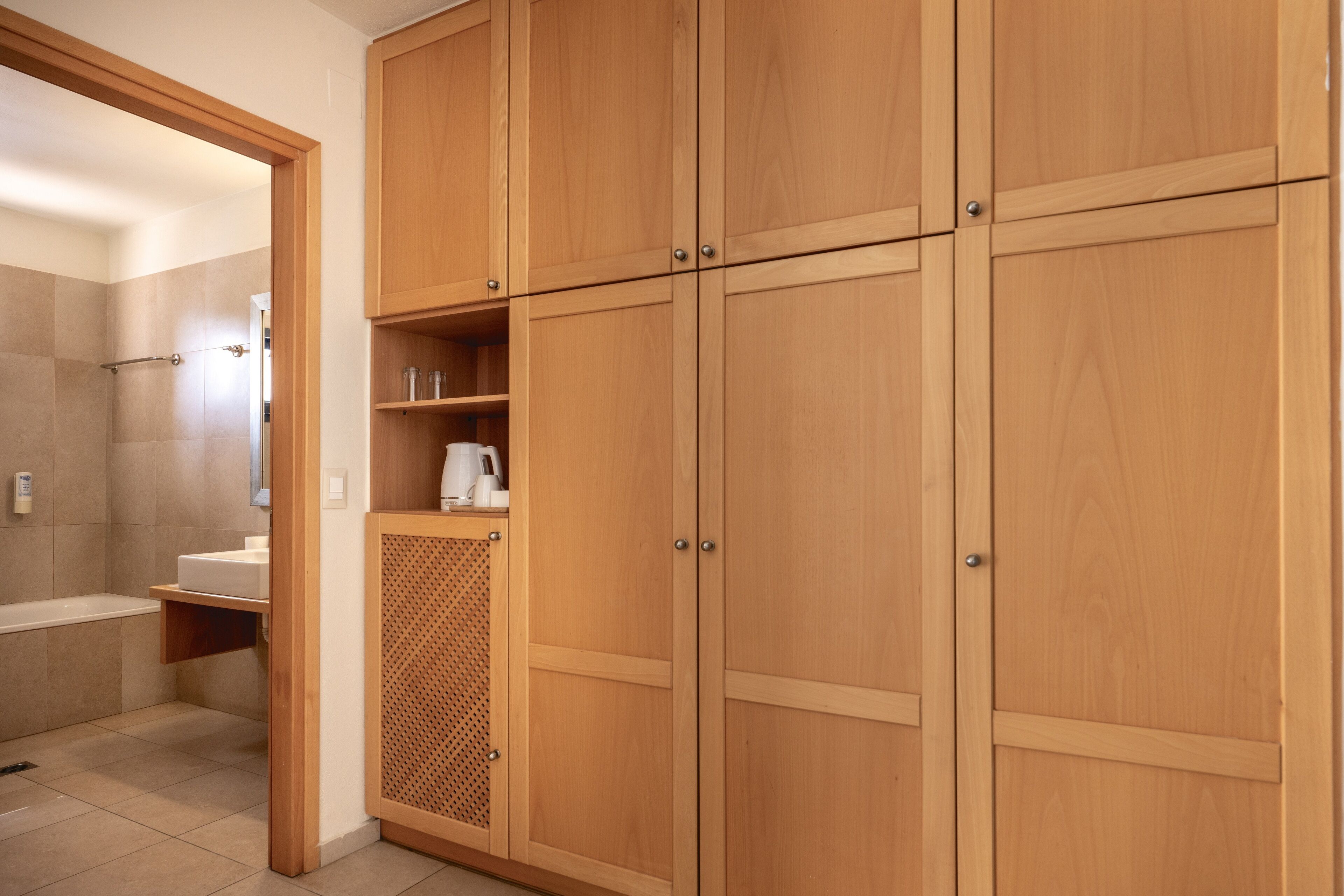 A wooden wardrobe with multiple doors and shelves, a bathroom with a bathtub and a shower area.