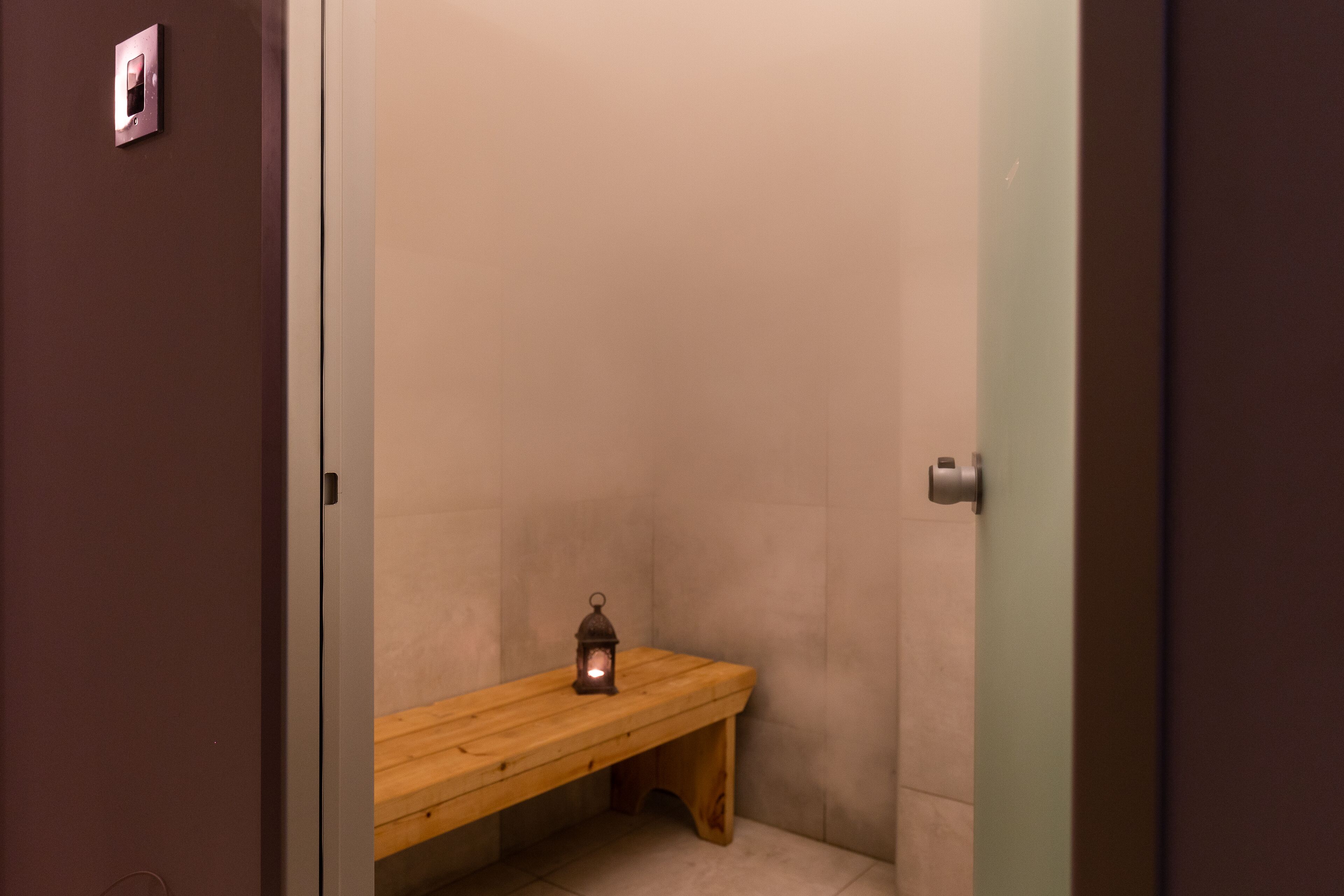 A small, dimly lit bathroom with a wooden bench and a single wall-mounted light fixture.