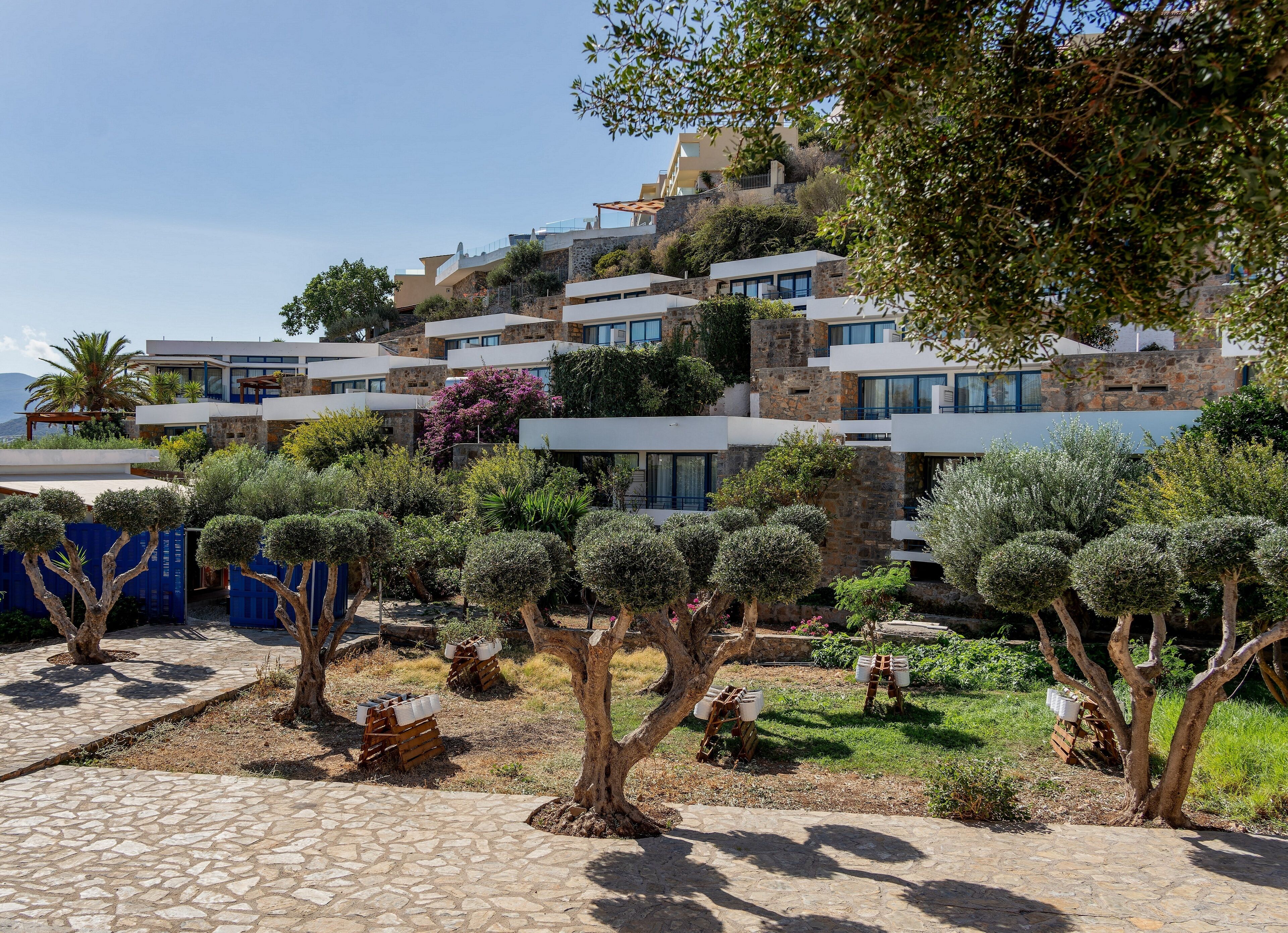 A hillside property with modern architecture, stone buildings, and a well-maintained garden with various trees and shrubs.