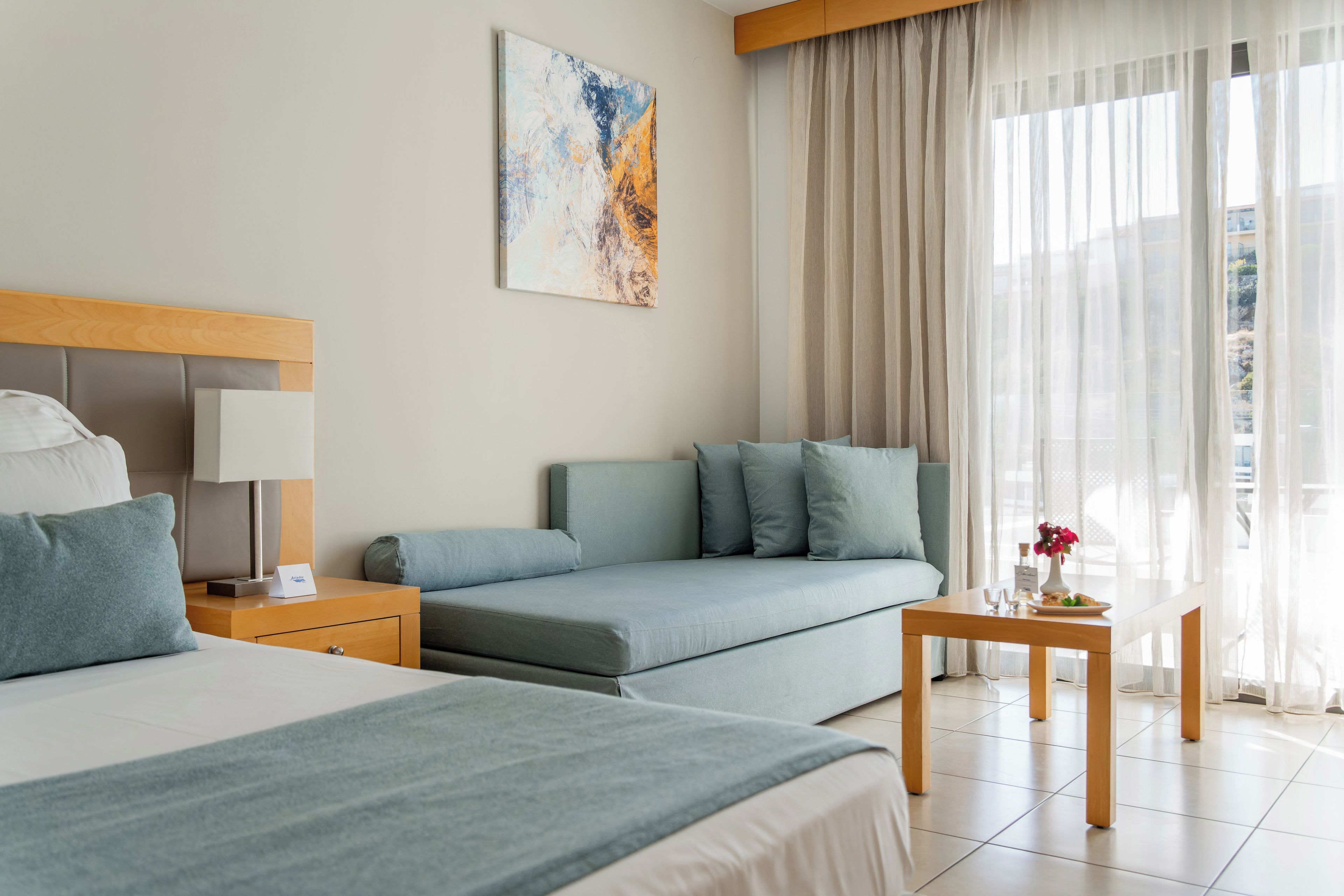 Una habitación de hotel con cama, sofá, mesita de noche y una mesa con un florero y un plato.