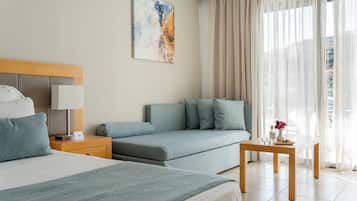 Una habitación de hotel con cama, sofá, mesita de noche y una mesa con un florero y un plato.