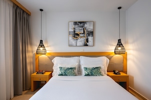 Una habitación de hotel con una cama grande, dos mesitas de noche, una obra de arte en la pared y dos lámparas colgantes.