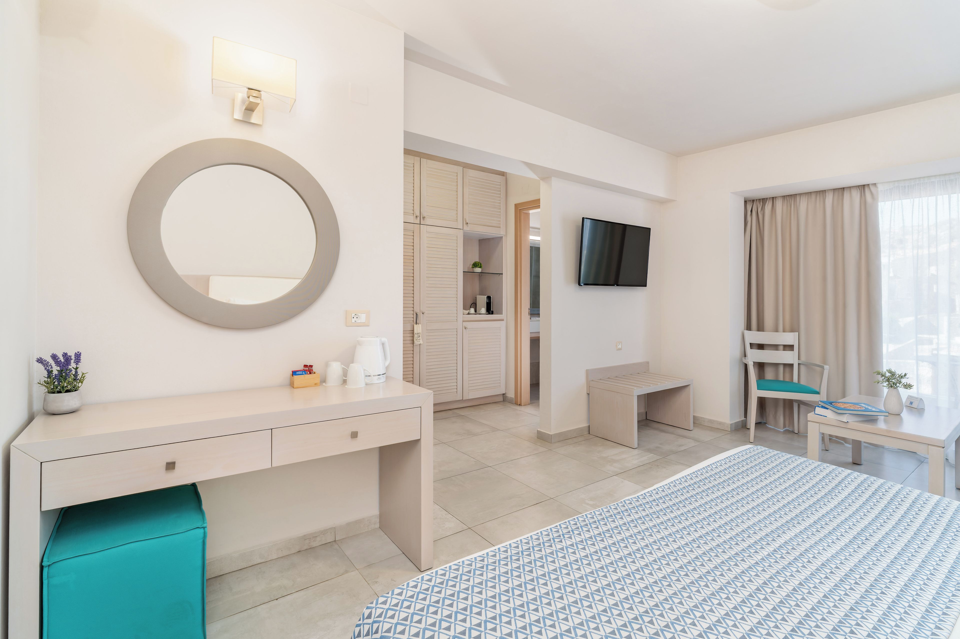 A hotel room with a bed, a desk, a TV, a mirror, and a bathroom visible through an open door.