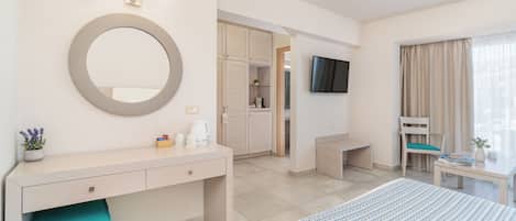 A hotel room with a bed, a desk, a TV, a mirror, and a bathroom visible through an open door.