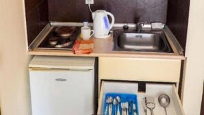 A compact kitchenette with a microwave, stove, sink, and storage drawers. - Kamari Apartments (Corfu)