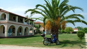 A building with a tiled roof, arched balconies, and a palm tree in the foreground. - Kamari Apartments (Corfu)