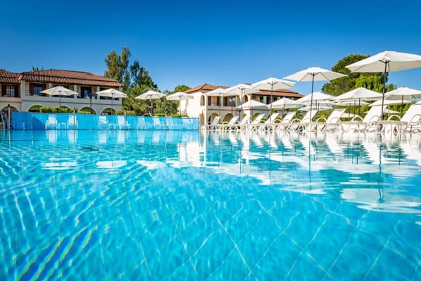 A clear blue swimming pool with lounge chairs and umbrellas, surrounded by buildings with red-tiled roofs. - Kamari Corfu Hotel & Apartments (Corfu)