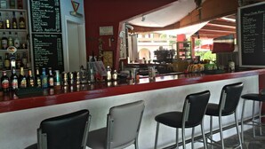 A bar area with a red counter, black and white chairs, and a menu board listing food and drink items. - Kamari Apartments (Corfu)
