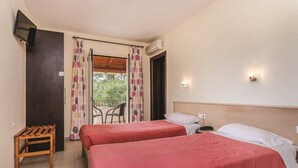 A hotel room with two beds, a small wooden table, a chair, and a balcony with curtains. - Kamari Apartments (Corfu)