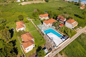 An aerial view of a property with multiple buildings, a swimming pool, and a large green field.