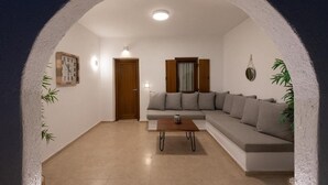 A living room with a sofa, a coffee table, a door, and a wall clock. - Edem Garden Residence (Mykonos)