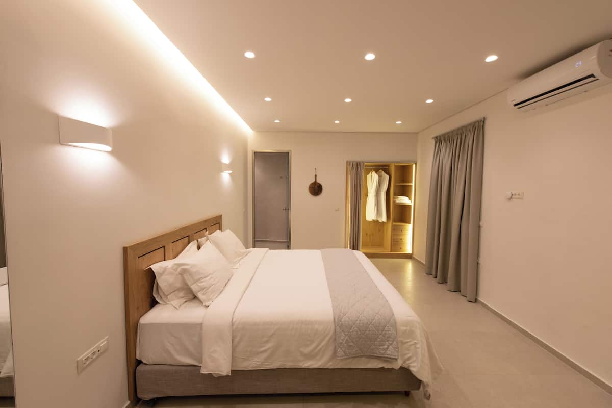 A modern bedroom with a wooden headboard, a bed with white bedding, a bedside table, and a wardrobe.