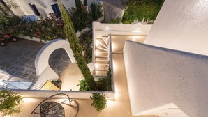 A modern building with a white exterior, a spiral staircase, and a small outdoor seating area with a metal chair and plants. - Edem Garden Residence (Mykonos)