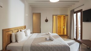 A neatly made bed with a quilted cover, a wooden headboard, and two rolled towels on the bed. - Edem Garden Residence (Mykonos)