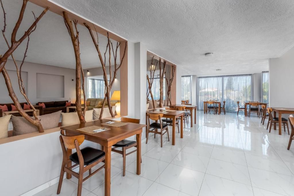 Un espace repas moderne avec des tables et des chaises en bois, un canapé et un mur décoratif orné de branches d’arbres.