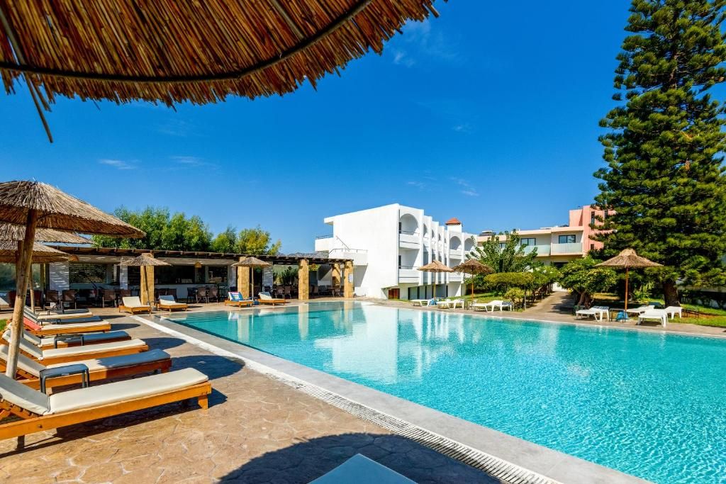 Ein Pool mit Liegestühlen und Sonnenschirmen, umgeben von Gebäuden und Grünpflanzen.