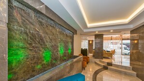 A lobby with a marble reception desk, seating area, and a large wall with a green light feature. - Bisetun Hotel (Istanbul)