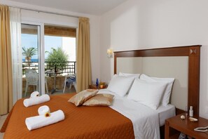 Quarto de hotel com uma cama grande, cabeceira de madeira, mesa de cabeceira e vista para o exterior através de uma porta de vidro deslizante.