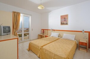 Una habitación de hotel con dos camas, televisión, una mesita y ventana con cortinas.