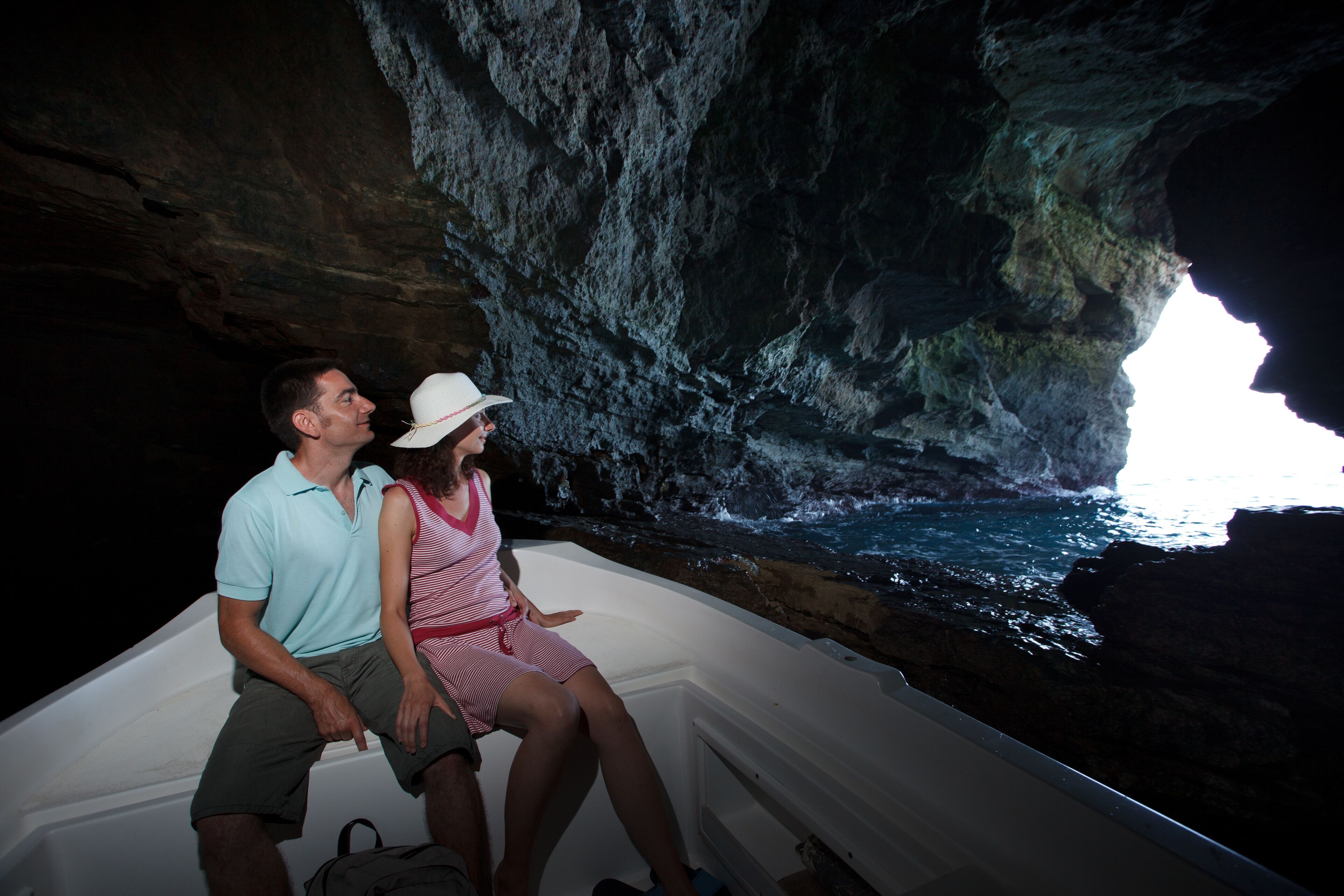 A couple in a boat inside a cave with a view of the ocean.