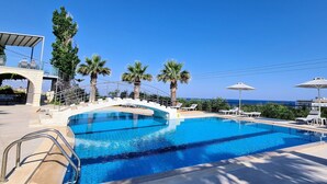 A swimming pool with a clear blue water, surrounded by palm trees and lounge chairs. - Oasis Scaleta Hotel (Rethymno)