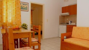 A compact kitchen with wooden cabinets, a dining table with chairs, and a sofa. - Matheos Apartments (Hersonissos)