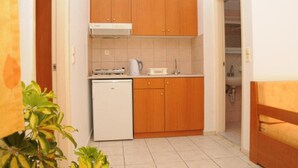 A compact kitchen with wooden cabinets, a white dishwasher, and a countertop with a kettle and toaster. - Matheos Apartments (Hersonissos)