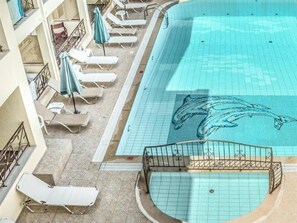 A swimming pool with a dolphin mural, lounge chairs, and a tiled deck. - Alexandros (SISSI)
