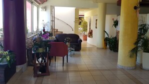 A spacious corridor with a staircase, potted plants, and a seating area with a sofa and armchairs. - Alexandros (SISSI)