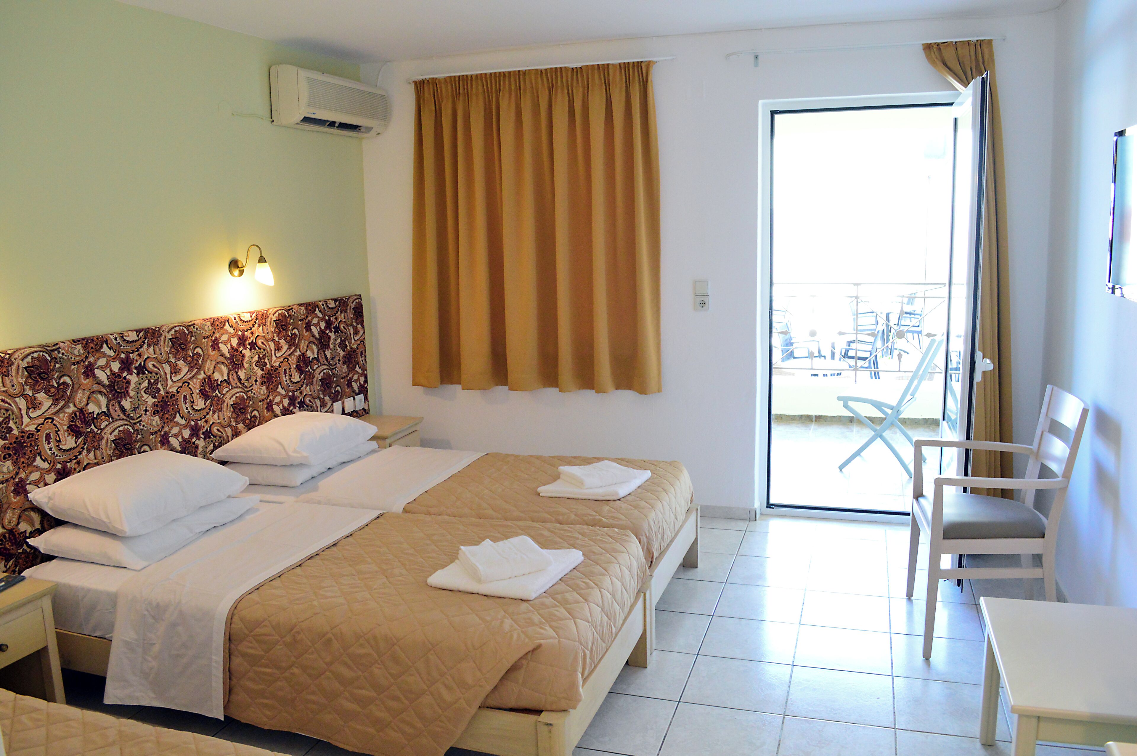 A hotel room with two beds, a patterned headboard, a balcony with a view, and a chair.