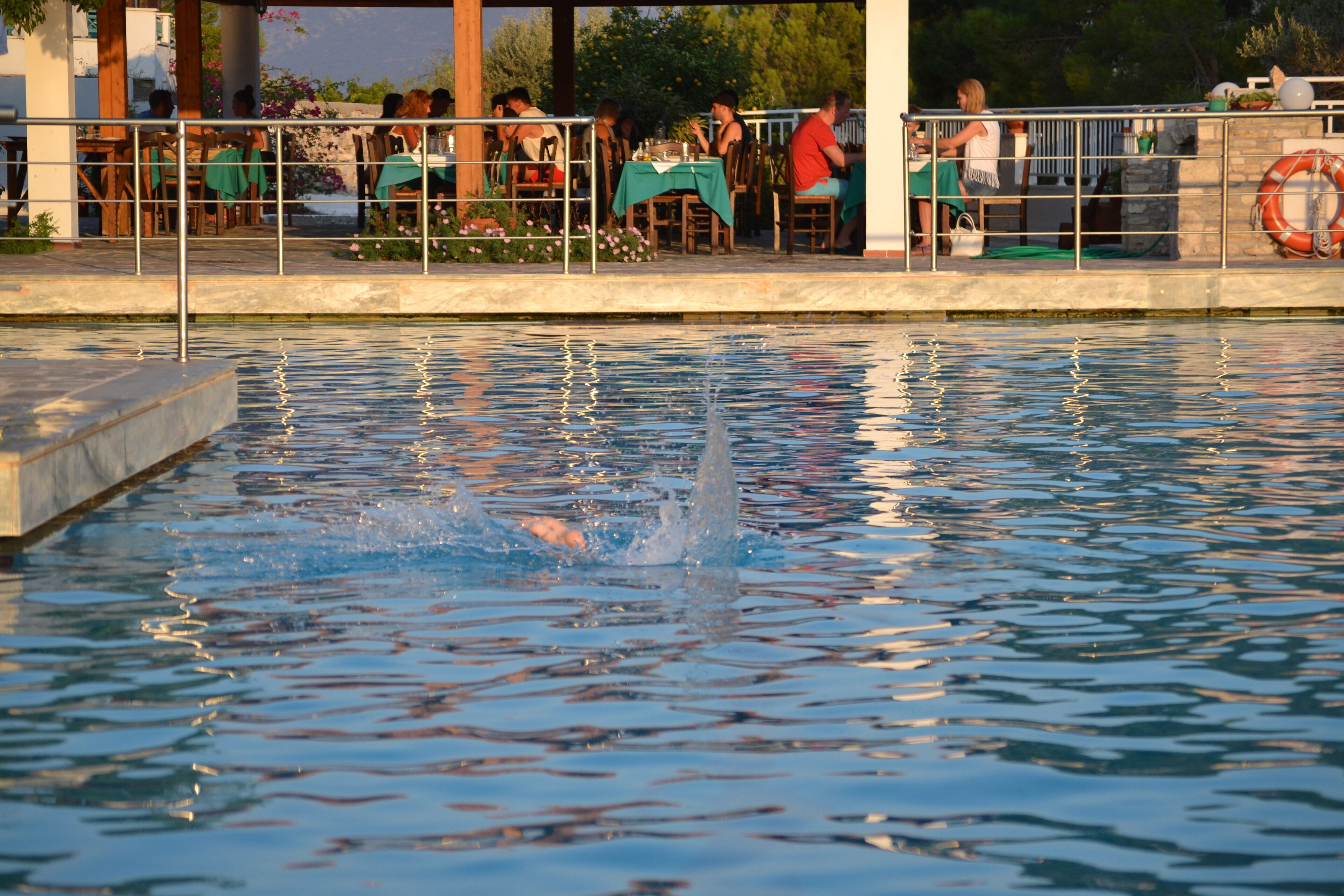 A swimming pool with people dining at tables in the background.