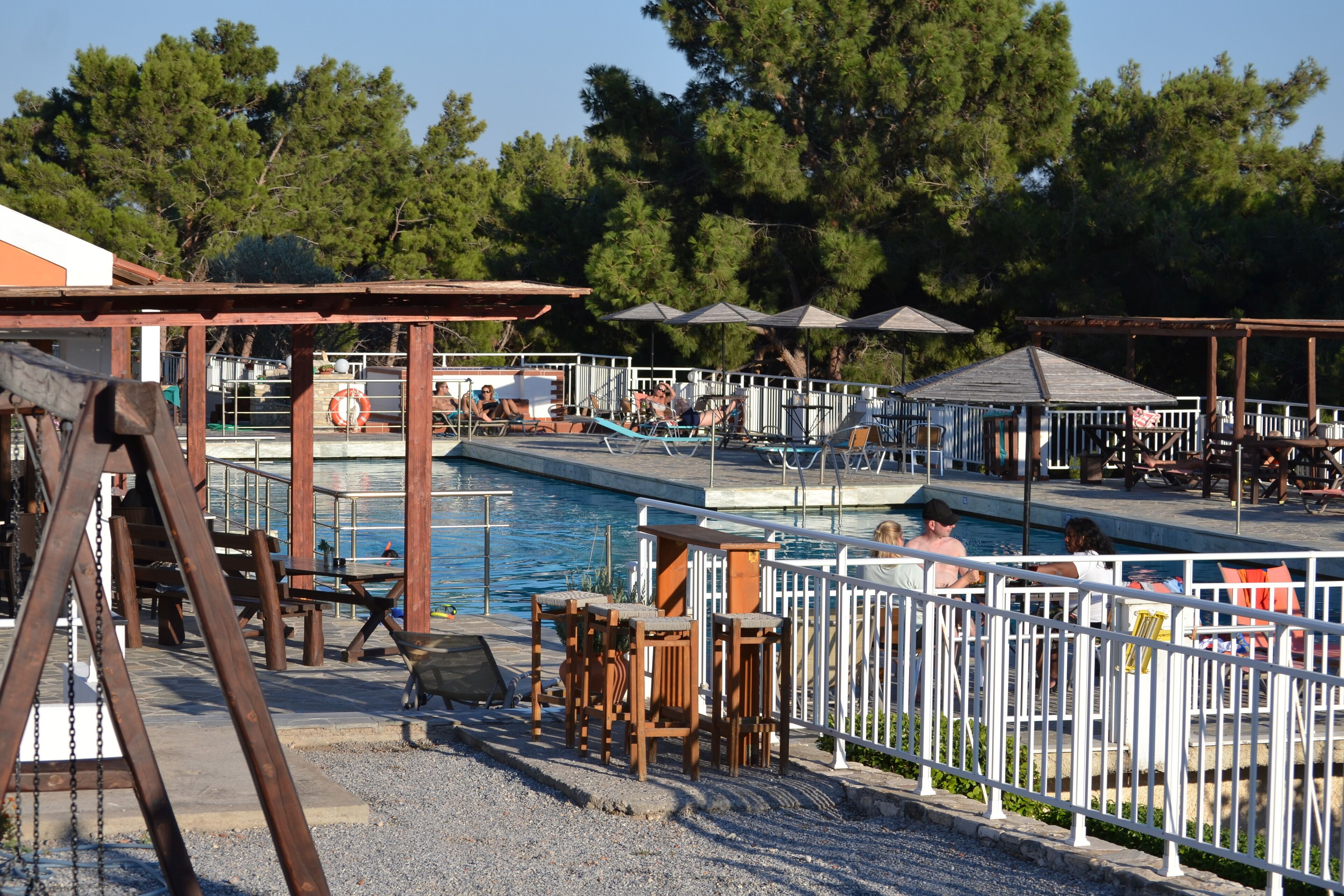 A poolside area with a wooden deck, lounge chairs, and a fenced swimming pool.