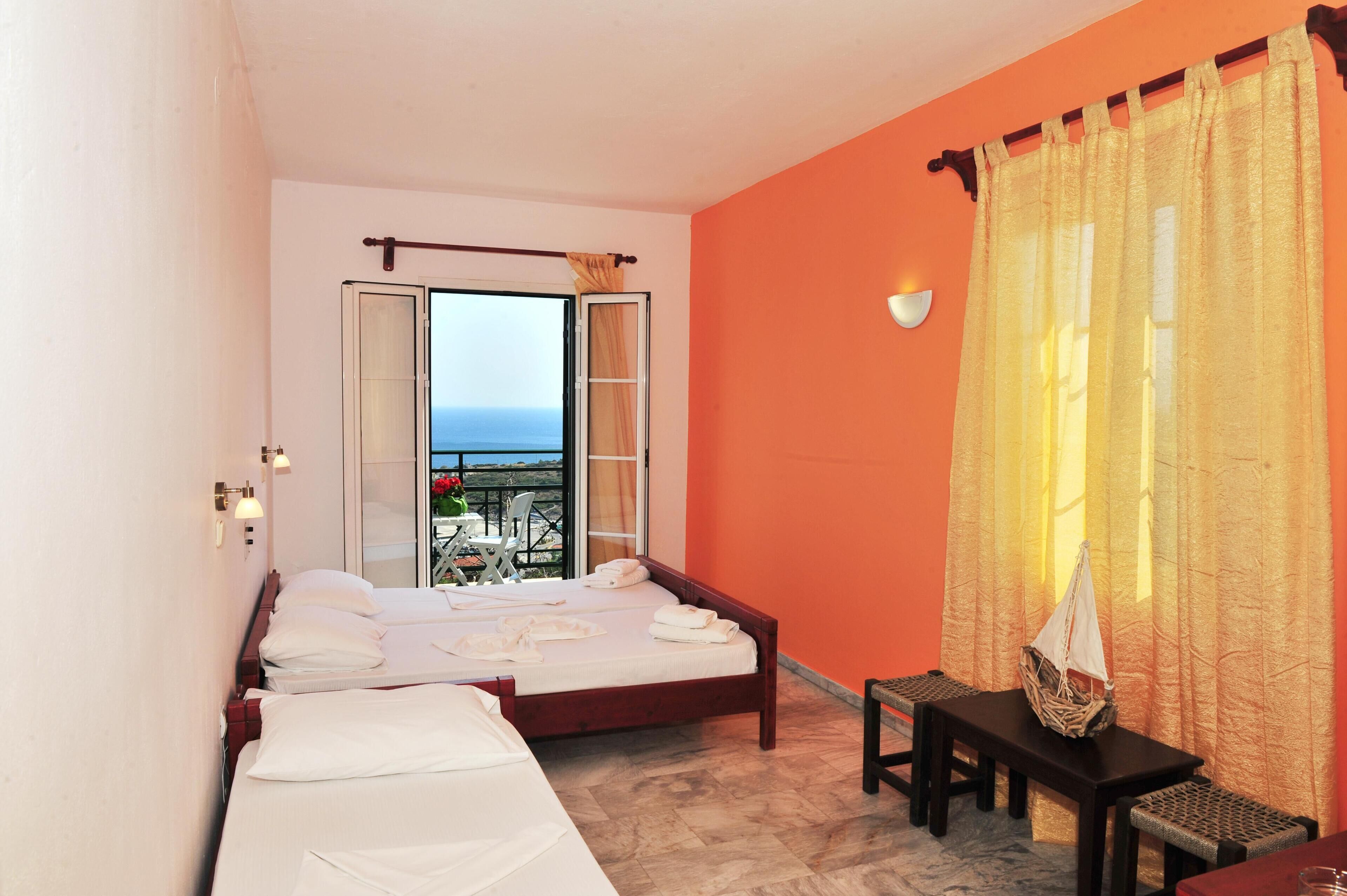A hotel room with two beds, a balcony with a view, and a table with a basket.