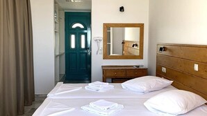 Habitación de hotel con dos camas, cabecera de madera, espejo, cómoda de madera y puerta color verde azulado.