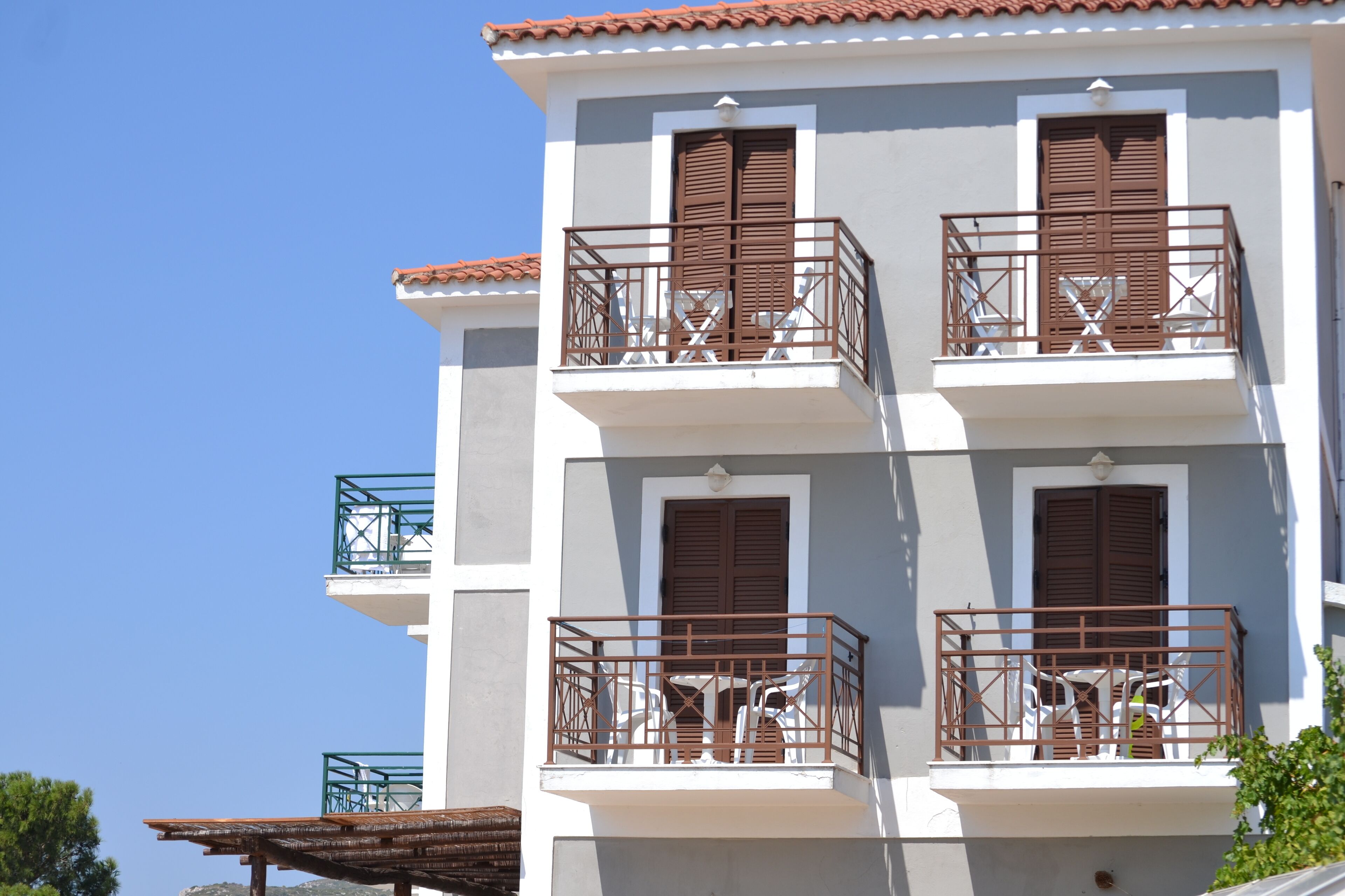Un immeuble à plusieurs étages doté de balcons, chacun étant agrémenté d’une rambarde en métal et de volets bruns.