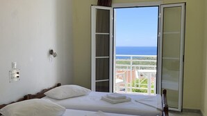 Habitación de hotel con dos camas, un balcón con vista al mar y una puerta corrediza.