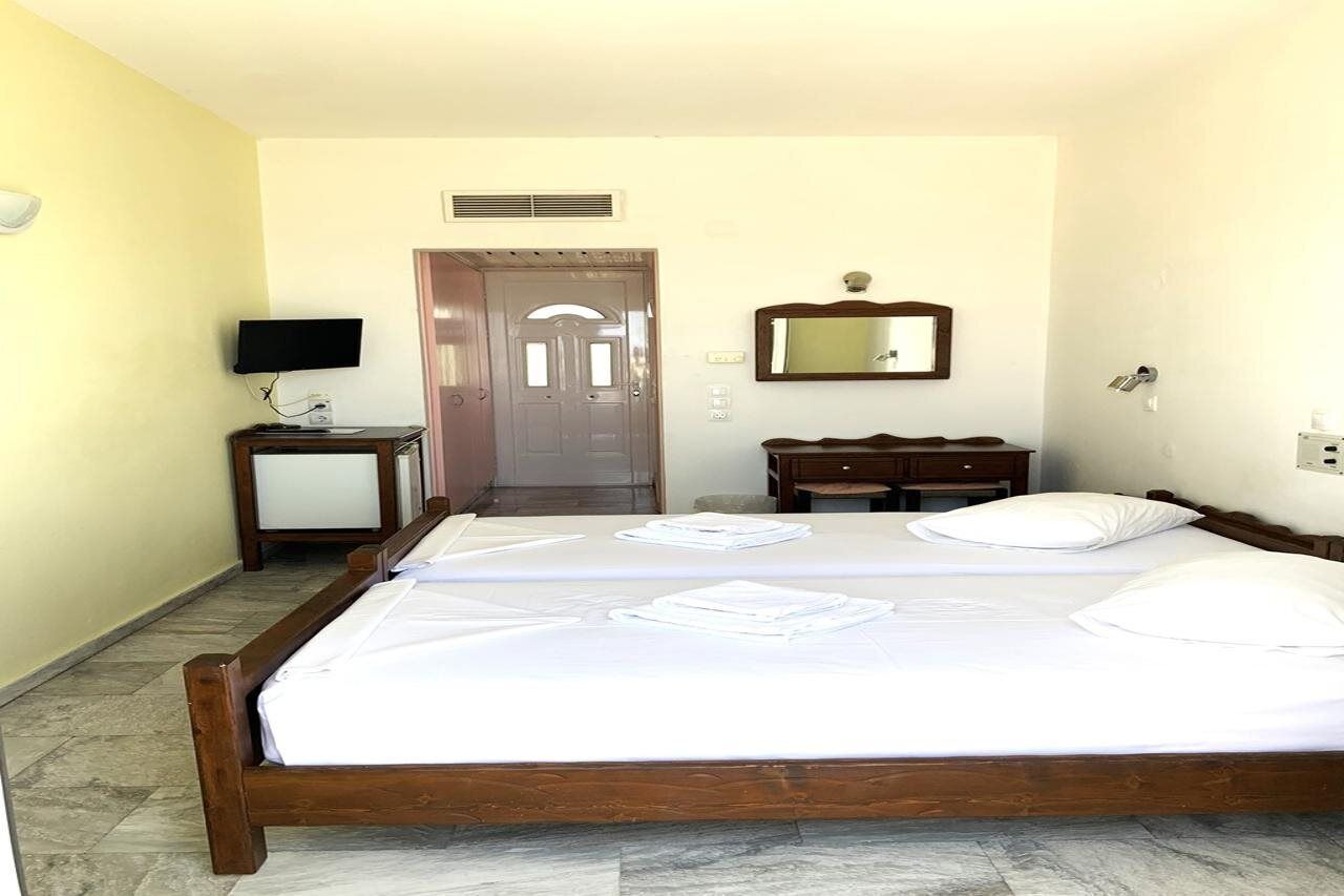 A hotel room with a large bed, a television, a mirror, and a door.