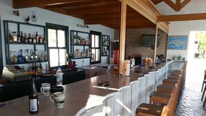Zona de bar con taburetes de madera, una barra larga y estantes llenos de botellas.