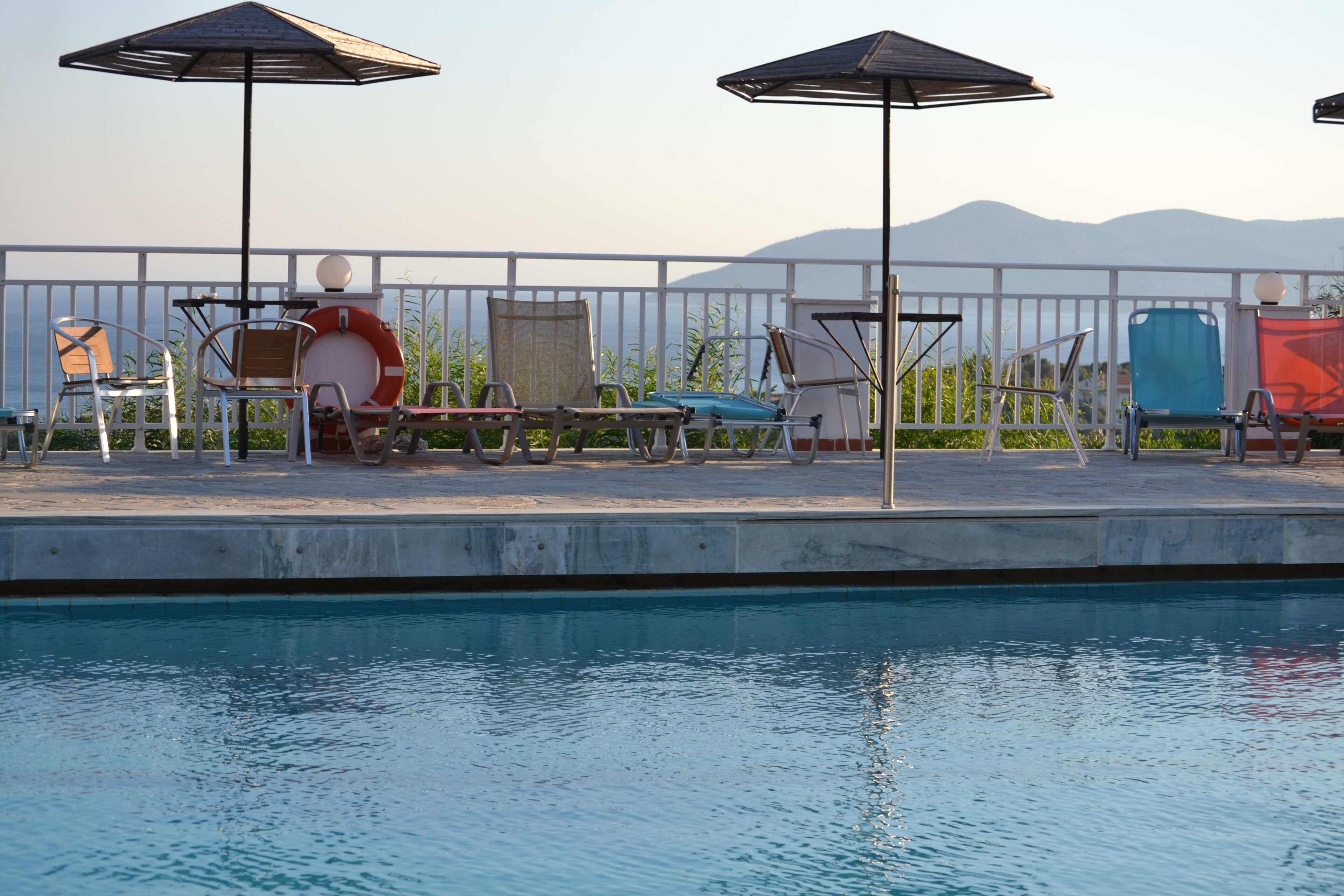 A poolside area with lounge chairs and umbrellas, a lifebuoy, and a view of mountains.