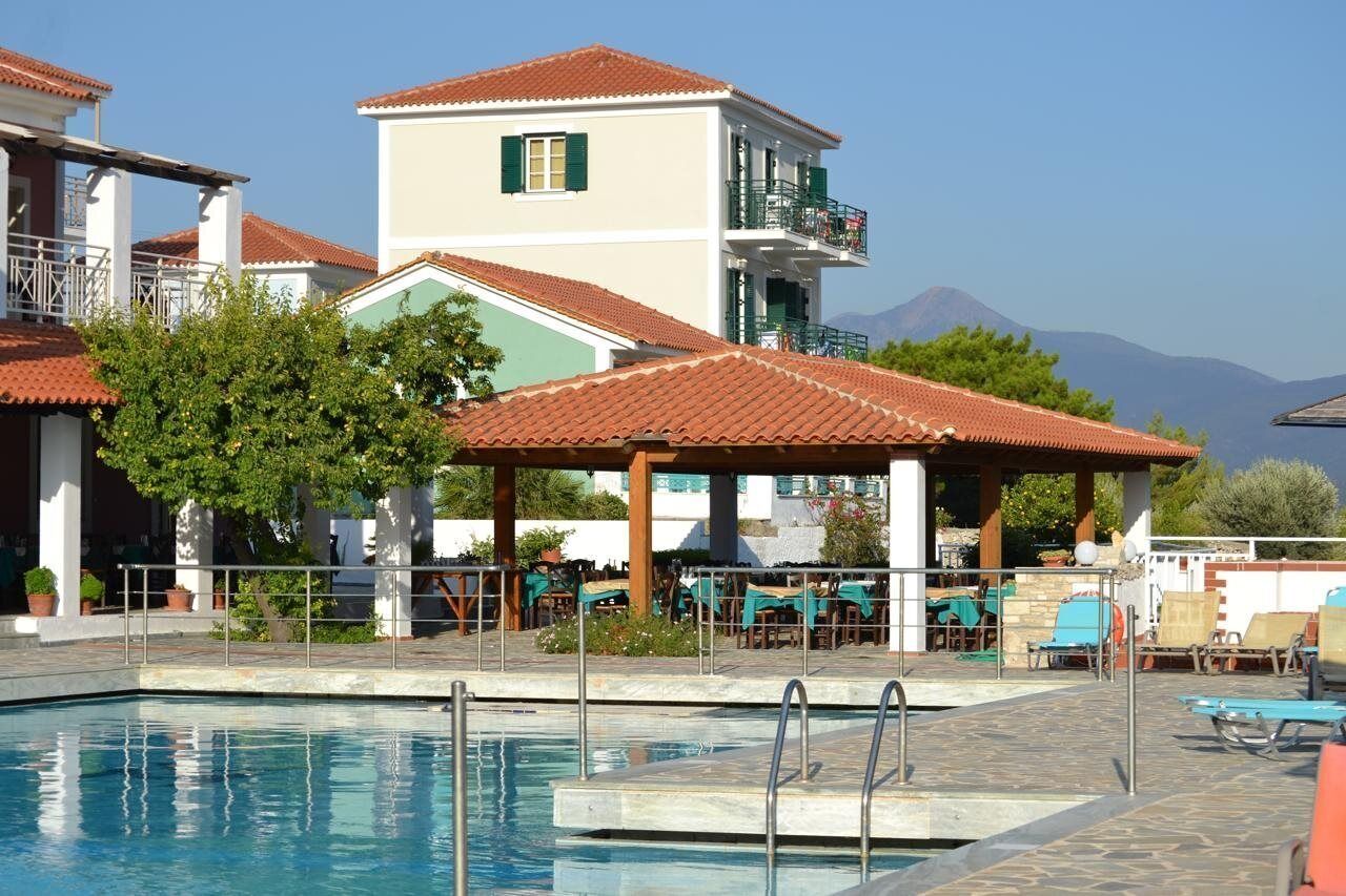A pool area with lounge chairs and a covered seating area, surrounded by buildings with red-tiled roofs and a mountain in the background.