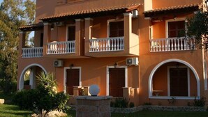 A two-story building with a balcony, arched windows, and a stone pillar in the foreground. - Vasso Studios (Corfu)