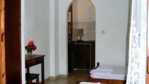 A room with two wooden beds, a wooden desk with a vase of flowers, and a small table. - Vasso Studios (Corfu)