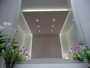 A modern interior with a recessed ceiling, white walls, and a central seating area. - Makis Louvlis Luxury Apartments (Corfu)