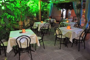An outdoor dining area with tables and chairs, covered by a pergola with green foliage. - Makis Louvlis Luxury Apartments (Corfu)