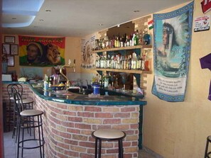Zona de bar con mostrador de ladrillo, taburetes y estantes llenos de botellas de licores.