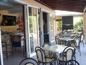 An outdoor patio area with tables and chairs, a television, and a sign for a sushi bar. - Makis Louvlis Luxury Apartments (Corfu)